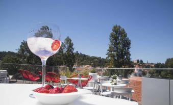 a large glass of white wine is on a table with strawberries and a bowl of strawberries in front of it at Thomar Boutique Hotel