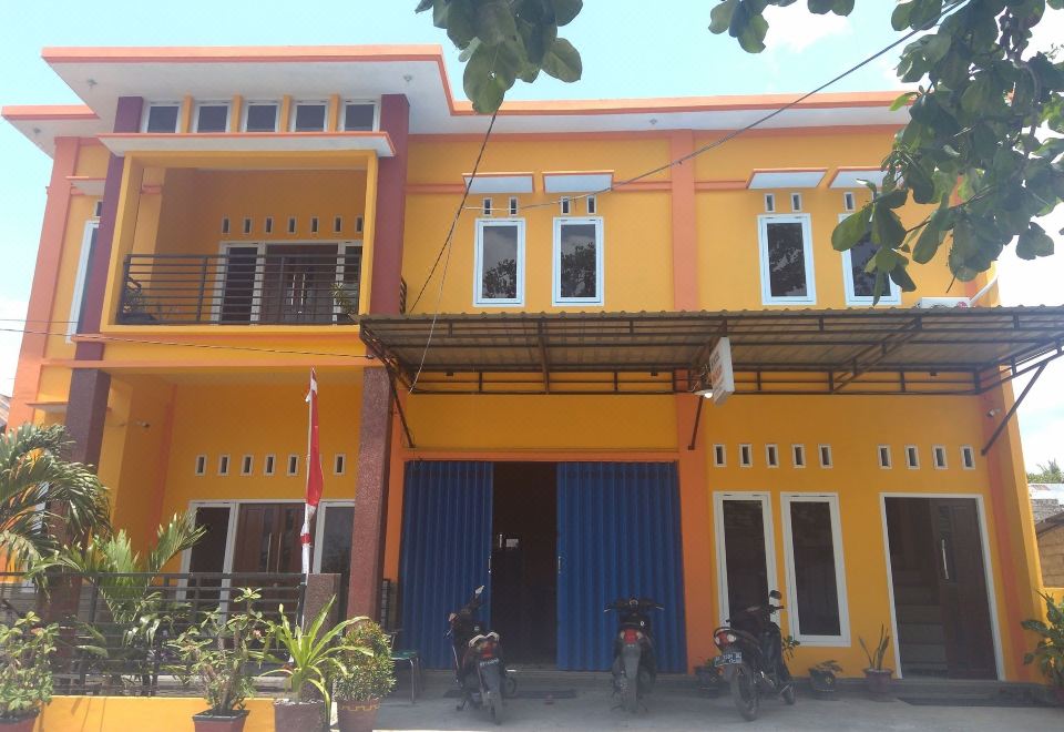 a yellow building with blue trim , two motorcycles parked outside , and a clear sky above at Sinar Harapan