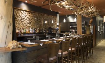 a well - lit restaurant with a long wooden bar , where several chairs and tables are arranged for dining at Hotel-Musee Premieres Nations