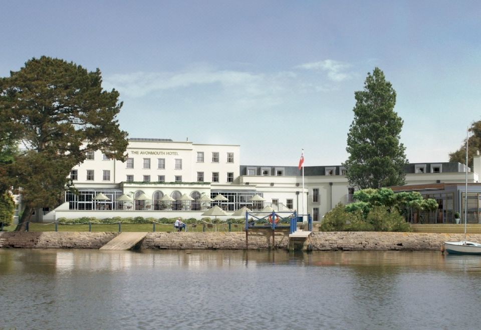 a large white building with a flagpole , surrounded by trees and a body of water at Harbour Hotel & Spa Christchurch