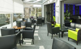 a modern lounge area with black leather chairs and tables , large windows , and sliding doors at Ibis Luxembourg Sud