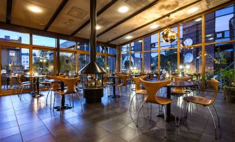 a modern restaurant with wooden tables and chairs , large windows , and a fireplace , bathed in natural light from the interior at Clarion Collection Hotel Carlscrona