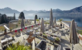a rooftop restaurant with outdoor seating , umbrellas , and a view of the mountains in the background at Alpenblick Weggis - Panorama & Alpen Chic Hotel
