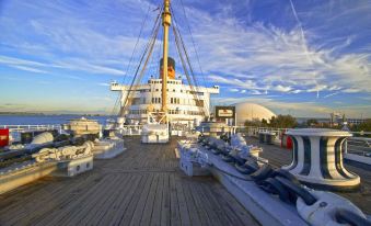 a large ship docked at a pier with several smaller boats and a clear blue sky at The Queen Mary