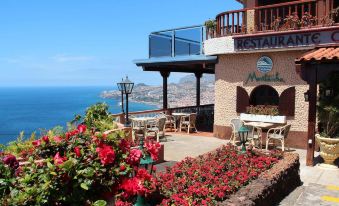 a restaurant with a view of the ocean , surrounded by red flowers and a balcony at Ocean Gardens