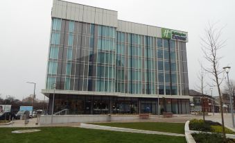 a large , modern building with a grassy area in front of it and the logo of a hotel on top at Holiday Inn Express Stockport