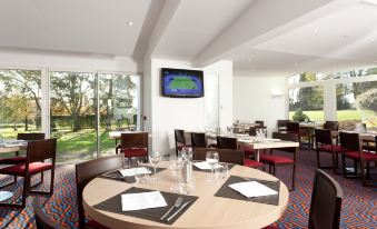 a dining room with a round table surrounded by chairs , and a tv mounted on the wall at Holiday Inn Lille - Ouest Englos