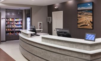a modern office reception area with a curved white counter , black chairs , and a sign on the wall at Residence Inn Provo North