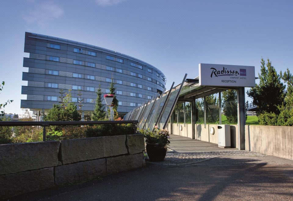 "a large , modern building with a sign reading "" radisson "" in front of it , surrounded by trees and plants" at Radisson Blu Airport Hotel, Oslo Gardermoen