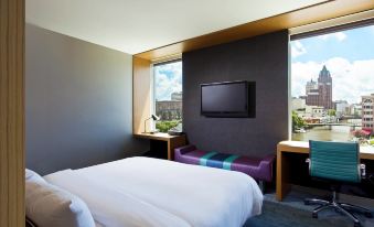 a hotel room with a large bed , a flat - screen tv mounted on the wall , and a window overlooking the city at Aloft Milwaukee Downtown