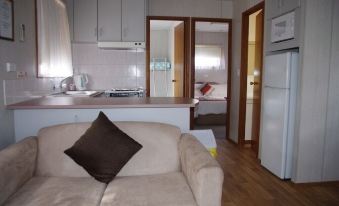 a living room with a couch , kitchen area , and kitchen visible through an open door at Deniliquin Pioneer Tourist Park