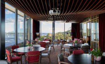 a large , open room with a high ceiling and floor - to - ceiling windows is filled with tables and chairs at Radisson Blu Caledonien Hotel, Kristiansand