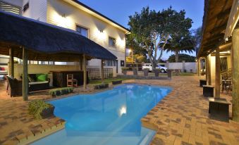 a beautiful backyard with a large swimming pool , patio furniture , and a thatched roof building at Balmoral Lodge