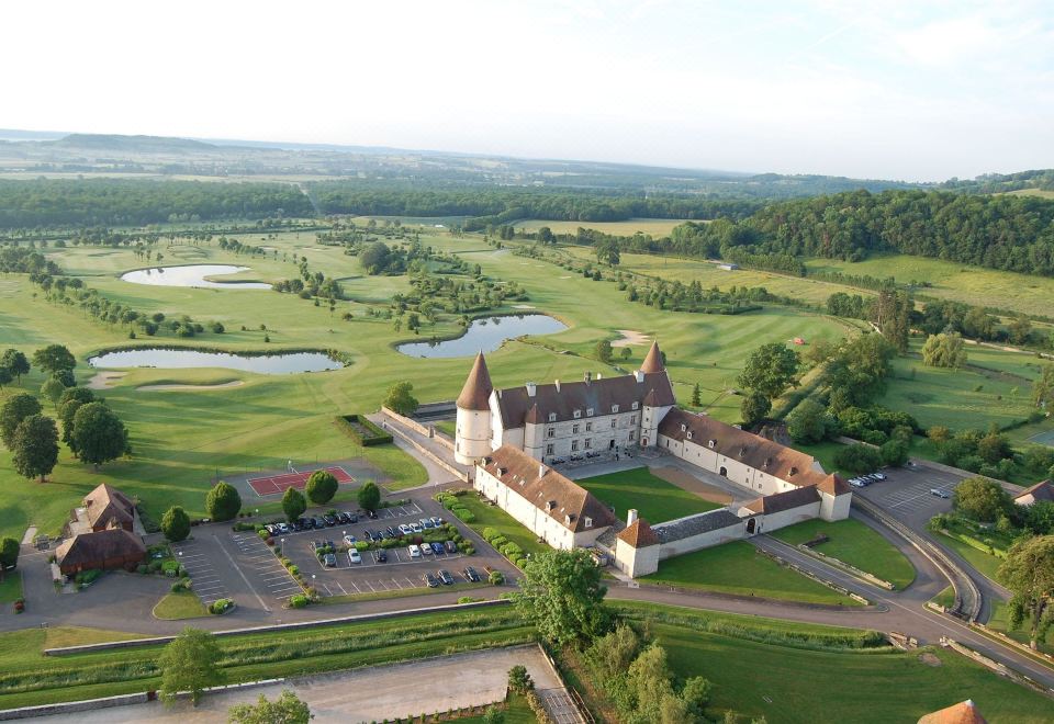 a large castle surrounded by a golf course , with cars parked in front of it at Hotel Golf Chateau de Chailly