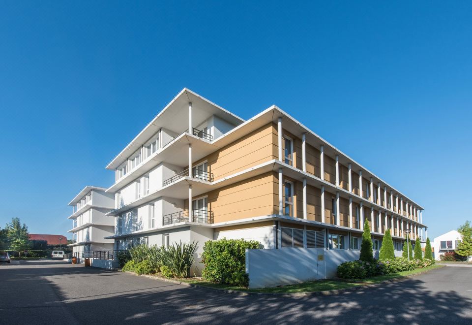 a modern , two - story building with a brown facade and white balconies under a clear blue sky at Comfort Suites Pau Idron