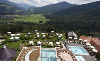 a large resort with multiple pools and a view of the mountains in the background at Alpin Panorama Hotel Hubertus