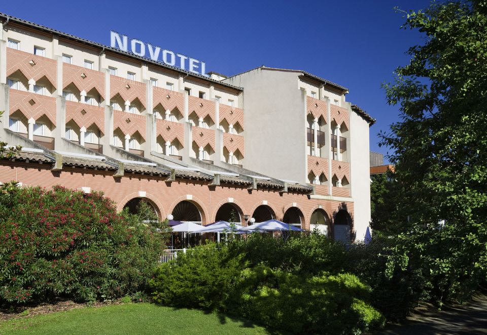 "a large , pink hotel with the word "" novotel "" on its roof , surrounded by lush greenery" at Novotel Toulouse Centre Compans Caffarelli