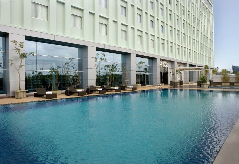 an outdoor swimming pool surrounded by a hotel , with several people enjoying their time in the pool at Novotel Bangka - Hotel & Convention Centre