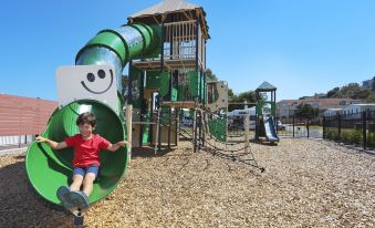 a young child is playing in a playground with a green slide and a play structure at Brighton Beachfront Holiday Park Adelaide