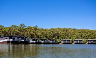 a row of houseboats on a body of water with trees in the background at Ingenia Holidays Lake Conjola