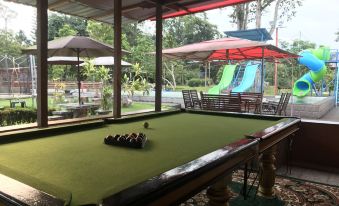 a billiards table set up in a covered outdoor area with umbrellas and trees in the background at Happy Paradise