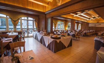 a large dining room with wooden tables and chairs , some of which are covered in tablecloths at Grand Hotel Misurina