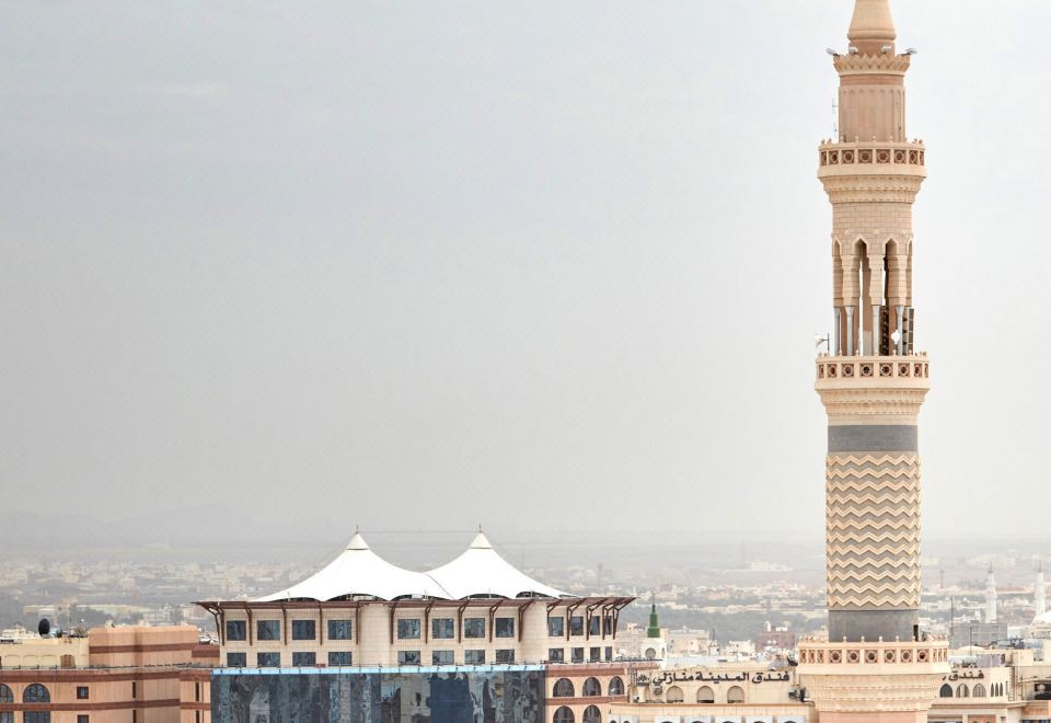 a tall , beige - colored building with a dome and minaret is surrounded by other buildings in the city at Pullman Zamzam Madina