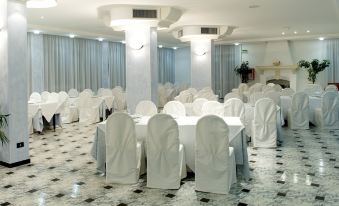 a large dining room with white tables and chairs , draped in white tablecloths , creating a formal atmosphere at Hotel Orsa Maggiore