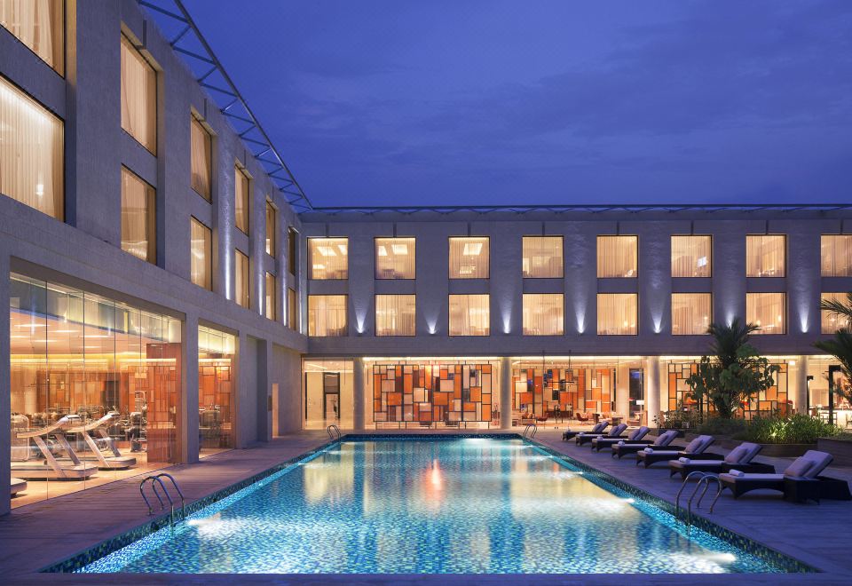 a large swimming pool is surrounded by lounge chairs and a building with many windows at Courtyard Kochi Airport