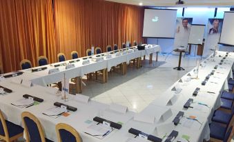 a conference room with rows of tables and chairs , a projector screen , and an empty podium at Hotel Panorama