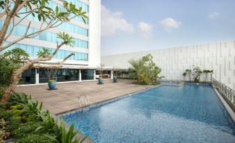 a large outdoor swimming pool surrounded by a building , with palm trees in the background at Holiday Inn Jakarta Kemayoran, an IHG Hotel