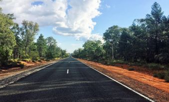 a long , empty road is seen in the middle of a red clay strip under a blue sky at Balonne River Motor Inn