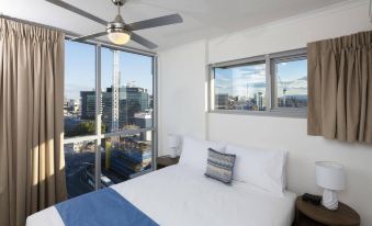 a bedroom with a bed , ceiling fan , and large windows overlooking a city view , including the sky at Direct Collective - Pavilion and Governor on Brookes