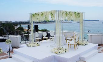 a wedding setup with a white and gold canopy , chairs , and flowers on an outdoor terrace overlooking the ocean at JW Marriott Cannes