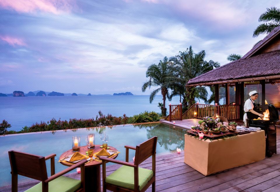a tropical setting with a wooden deck , table setting , and ocean view , accompanied by a boat on the water at Six Senses YAO Noi