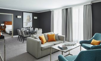 a modern living room with a gray couch , blue chairs , and a dining table in the background at London Heathrow Marriott Hotel