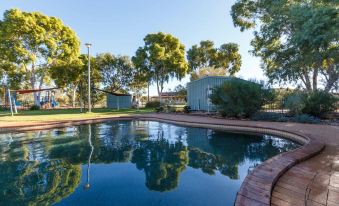 a large pool surrounded by trees and a wooden fence , with a building in the background at Discovery Resorts - Kings Canyon