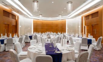 a well - decorated banquet hall with multiple round tables , white tablecloths , and chandeliers , set for a formal event at Radisson Blu M'Bamou Palace Hotel, Brazzaville