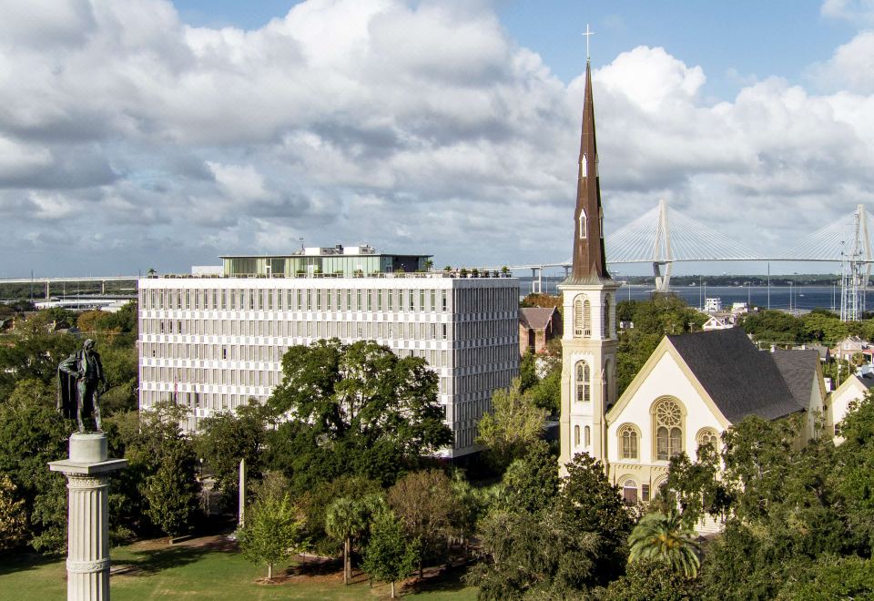a cityscape with a tall white church and a building in the foreground , surrounded by trees and other buildings at The Dewberry Charleston