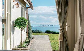 a house with a view of the ocean , and a room with curtains drawn on the window at Mudbrick Cottages
