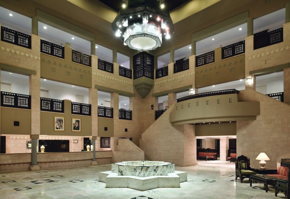 a large , open atrium with a chandelier hanging from the ceiling and a marble fountain in the center at Grand Mercure Petra