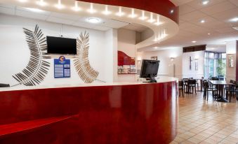 a hotel lobby with a red reception desk and chairs , creating a warm and inviting atmosphere at Comfort Hotel Montlucon