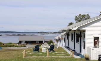 a white house situated next to a body of water , with chairs and a table placed in front of it at Friars Bay Inn & Cottages