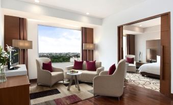 a living room with a large window , wooden floors , and white furniture , including two armchairs and a coffee table at Hyatt Centric Janakpuri New Delhi