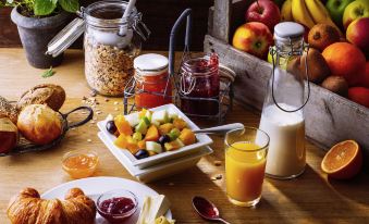 a wooden table is set with a variety of breakfast items , including fruit , cereal , juice , and milk at Ibis Sydney Airport