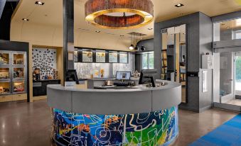 a modern hotel lobby with a large curved reception desk and colorful graffiti on the wall at Aloft Chapel Hill