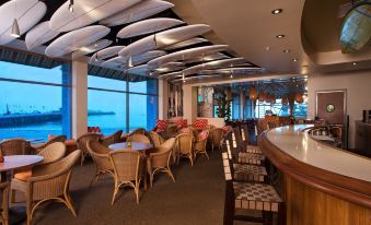a large room with wooden tables and chairs , a bar , and surfboards hanging from the ceiling at Dream Inn Santa Cruz