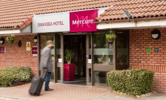 "a man is pulling a suitcase as he walks towards the entrance of a hotel named "" mercure swansea hotel .""." at Mercure Swansea Hotel