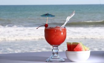 a refreshing drink with a cherry and umbrella garnish is placed on a table near the ocean at Hotel Estero y Mar