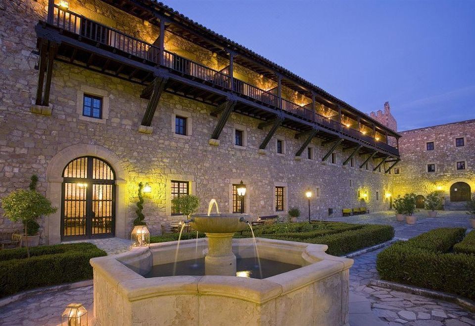 a courtyard with a fountain in the middle , surrounded by a stone building and lit up at night at Parador de Siguenza